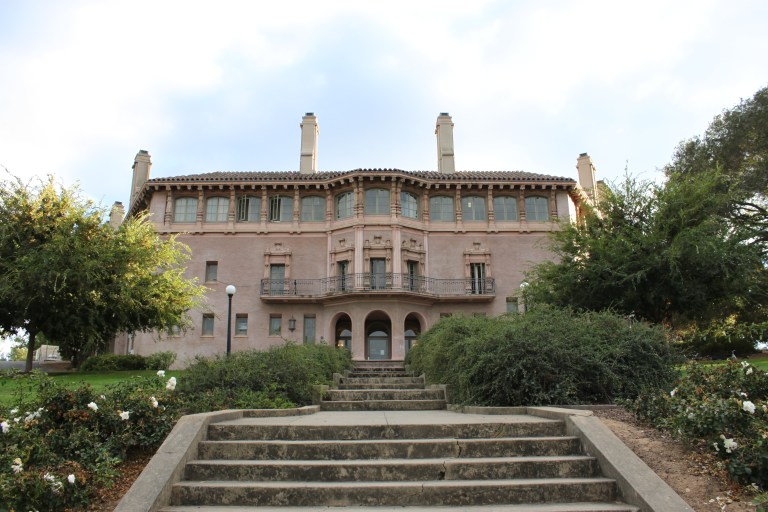 The Knoll building surrounded by trees and shrubs, along with a concrete staircase leading up to its entrance.