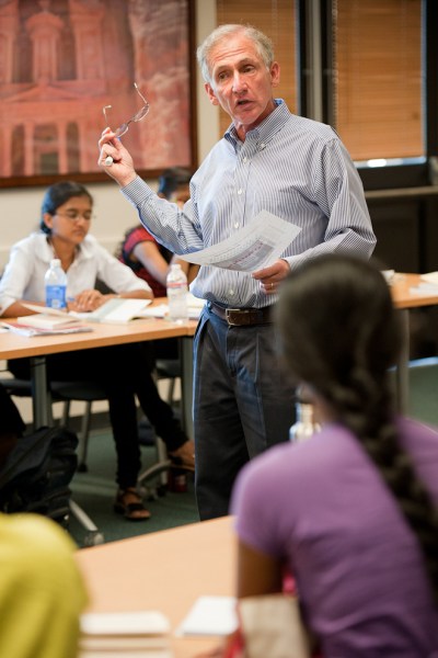 Picture of a professor in the middle of multiple tables teaching in-person class