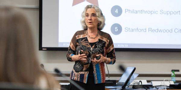 woman talks in front of a projected onto screen in front of a crowd