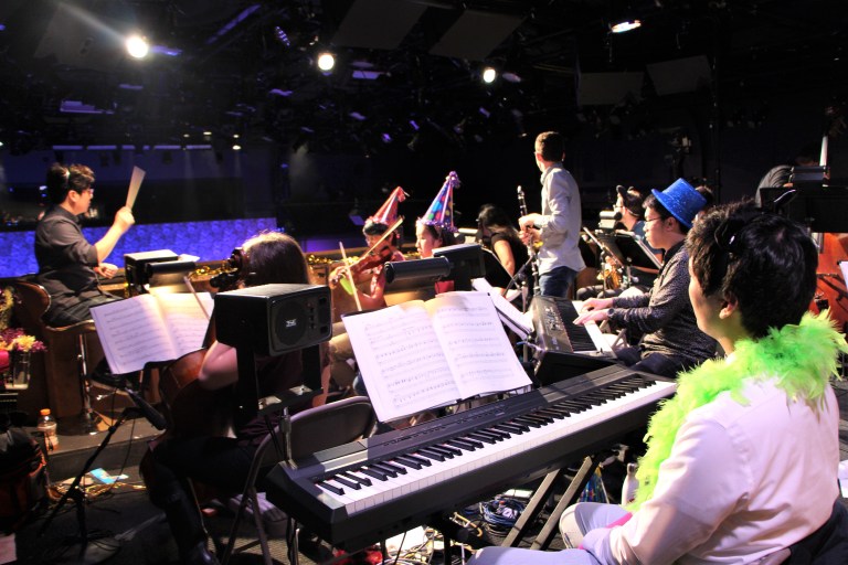 Chris Yoon ('19) conducts the fourteen-person "Cabaret" orchestra, decked out in party hats (THERESE SANTIAGO/The Stanford Daily).