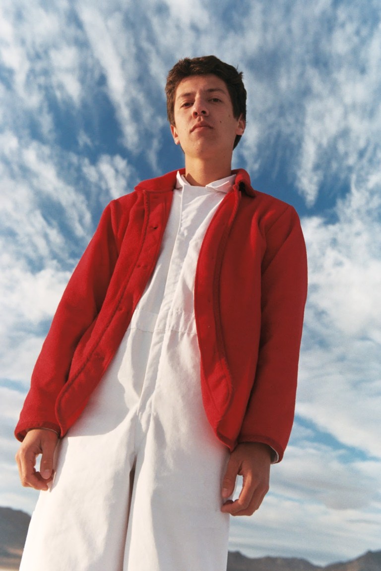 San Diego musician and visual artist Postcard Boy. He stands against a cloudy blue sky.