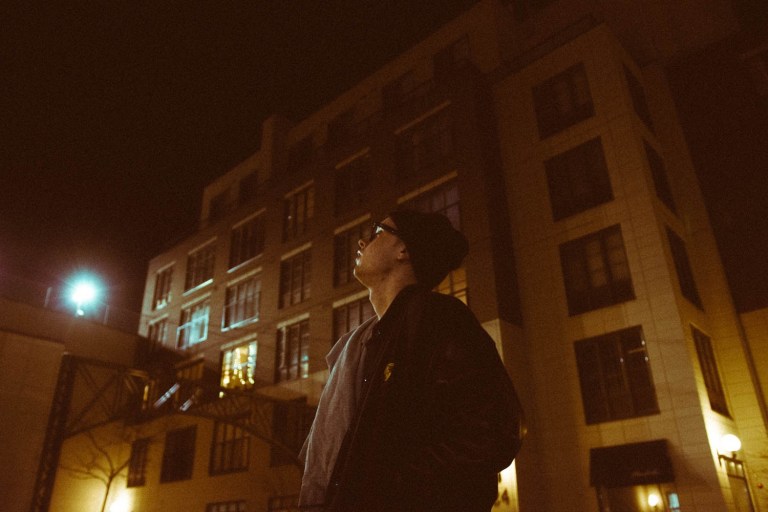 Erich Mrak is bundled up in a jacket and beanie, staring pensively off screen. The backdrop is a city at night.