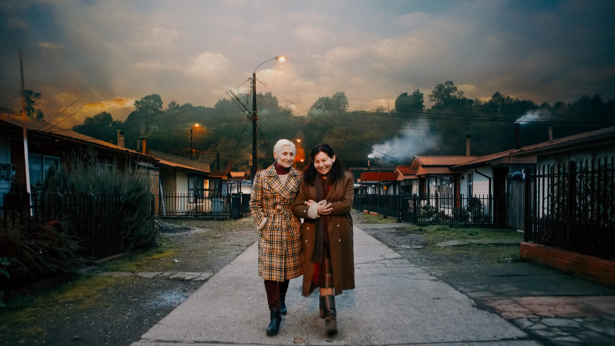 two older women walk down a road holding hands