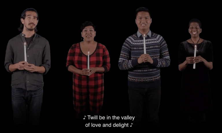 Four people holding candles singing against a black background