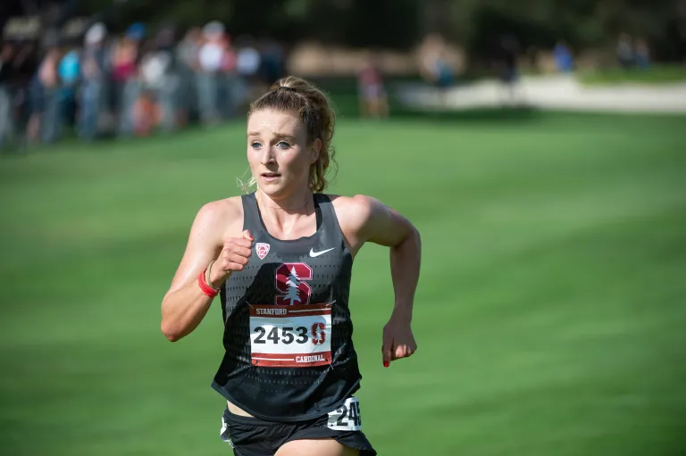 Elise Cranny running with a field of grass behind her.