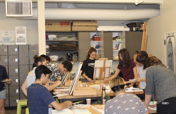 Students engage in artistic activities around a wooden table at the Roble Arts Gym