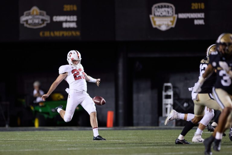 Ryan Sanborn prepares to punt a ball on a football field.