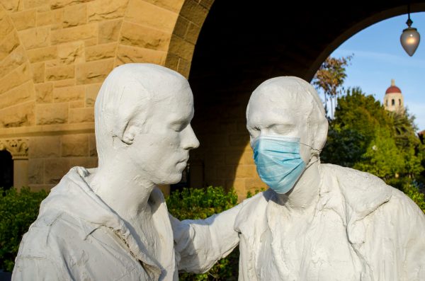 A photo of two statues on stanford's campus with one wearing a blue surgical mask