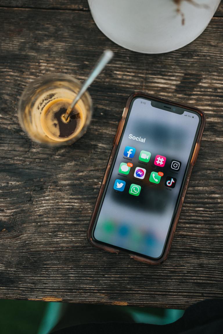 an iced Americano with a steel straw next to an open iPhone showing a group of social media apps