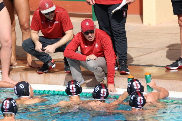 John Vargas kneels along the edge of the pool to speak to men's water polo players.