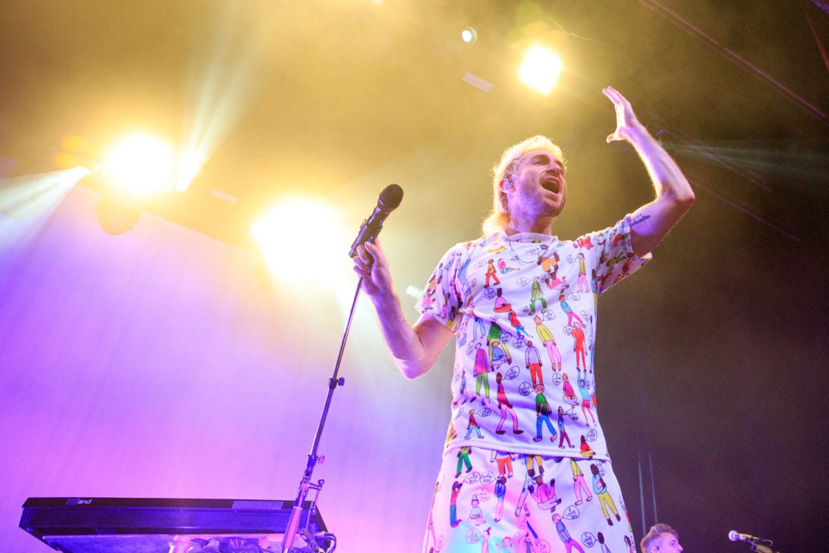 Medium image of Nicholas Petricca singing with his hand outstretched on a gold and purple-lit stage.