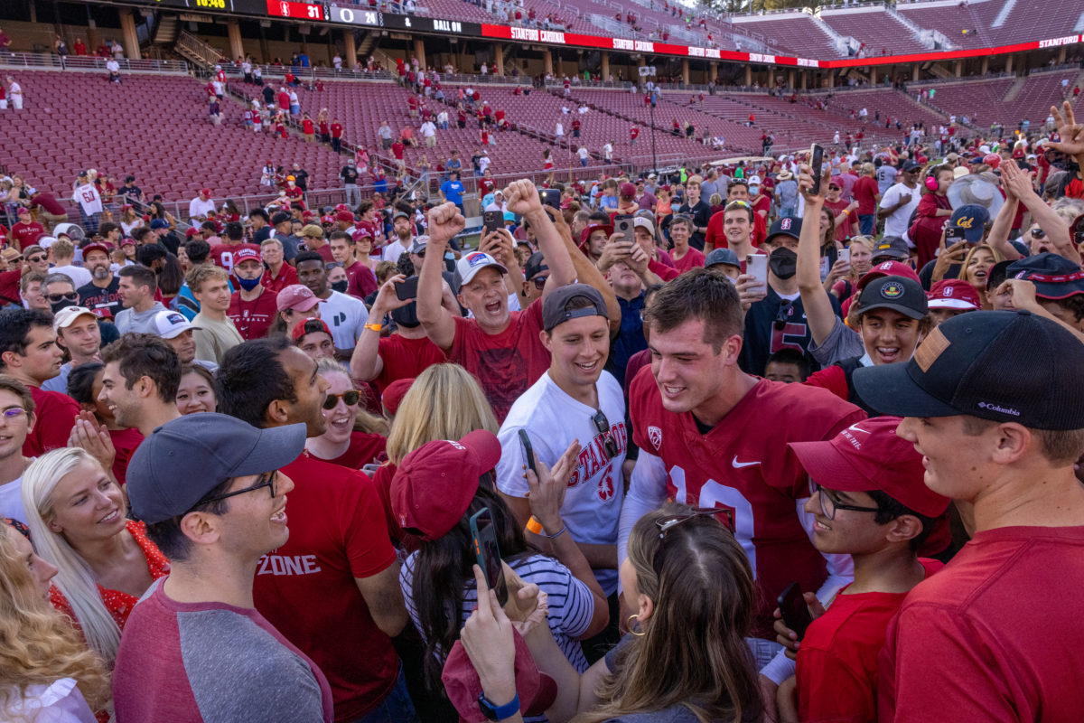 A crow of students surround sophomore quarterback Tanner McKee on the field. Some cheer and have their arms in the air. The seats of the stadium are now close to empty as the field fills with people.