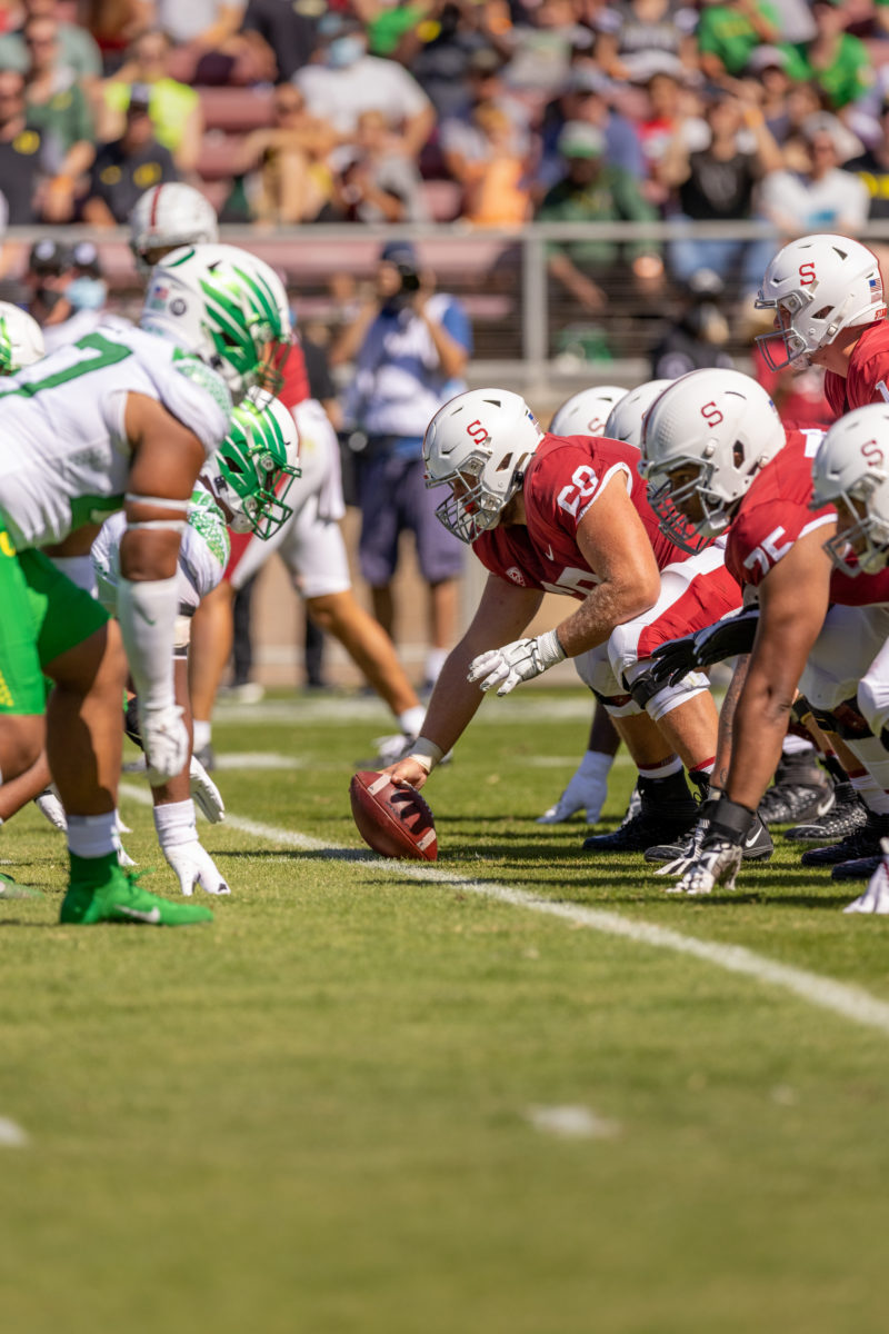 Oregon football players crouch on the left, while Stanford football players crouch on the right. One Stanford football player holds the football on the ground.