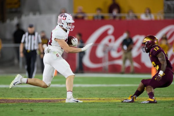 A football player runs down the field with the football with an opposing team player in front of him.