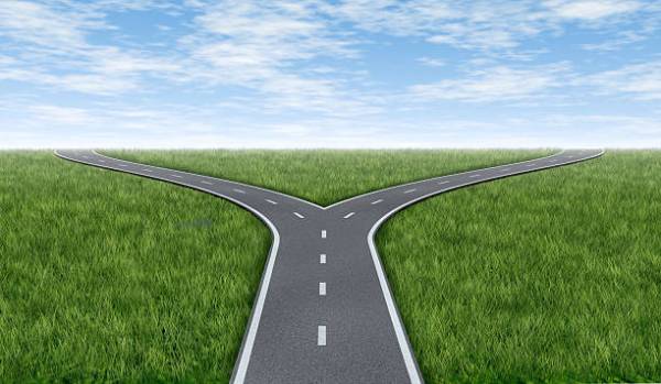 A fork in the road with a partly cloudy sky in a field of grass