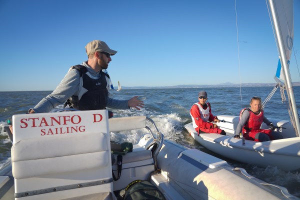 A man on a sailboat speaks to another man in a nearby sailboat.