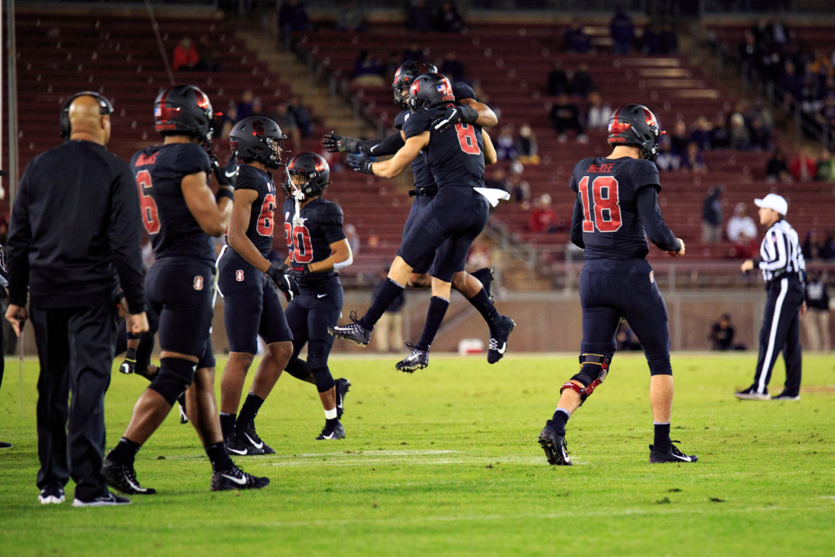 Stanford football players jump up in celebration on the field, with other players walking into the frame. 