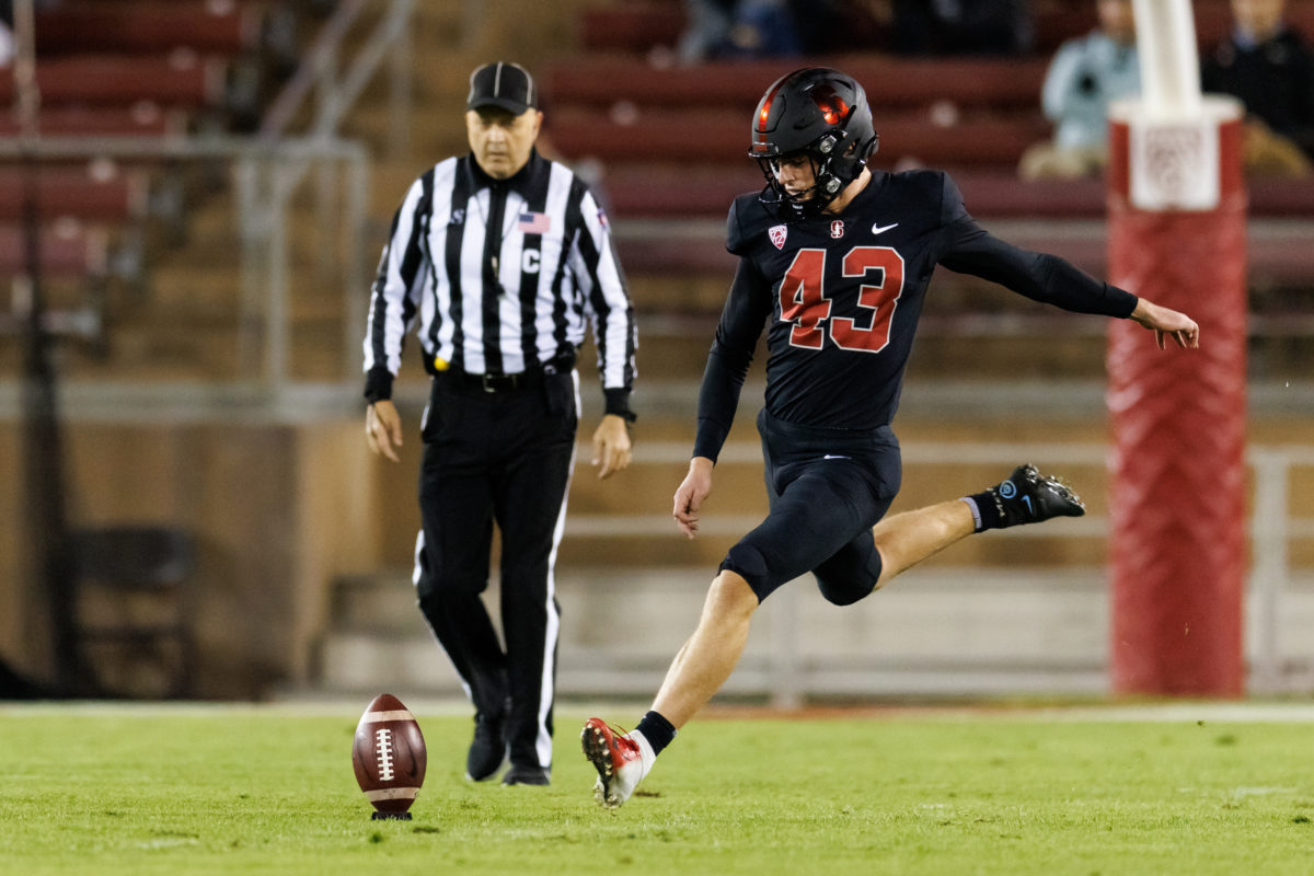 Stanford football player getting ready to kick football placed on the grass with referee behind him. 