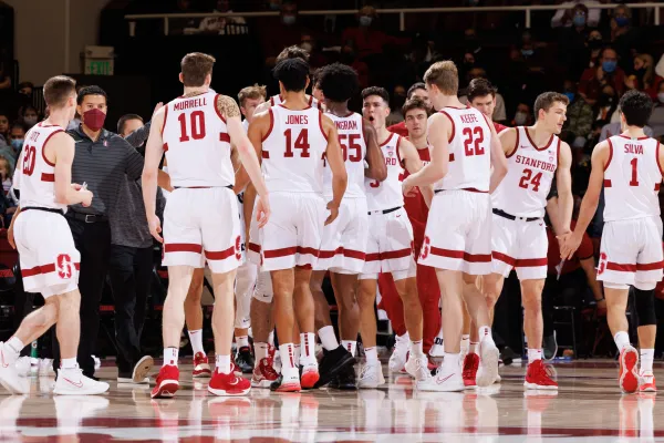 Stanford men's basketball stand in a huddle on the sideline.