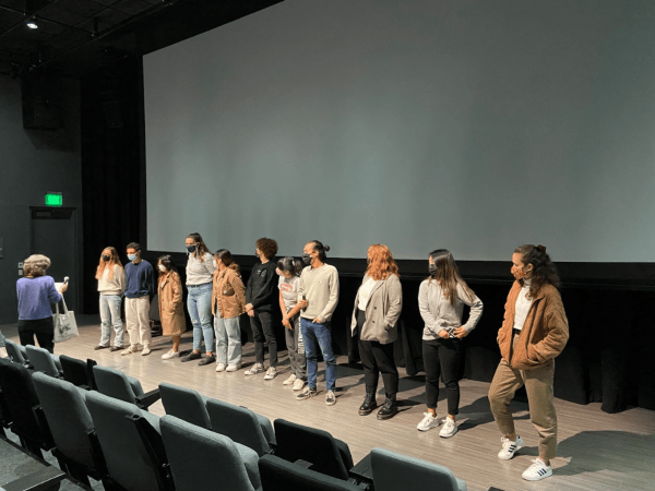 Students stand on stage in front of a projector screen.