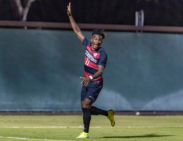 A soccer player runs down the pitch with his arm up, celebrating a play.