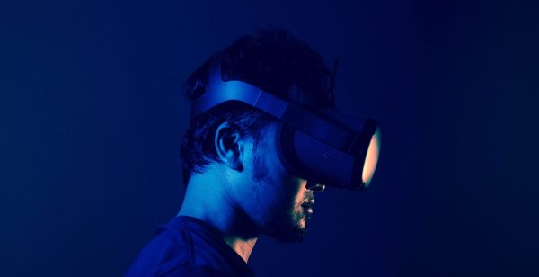 A man wears a virtual reality headset, facing to the right under blue light.