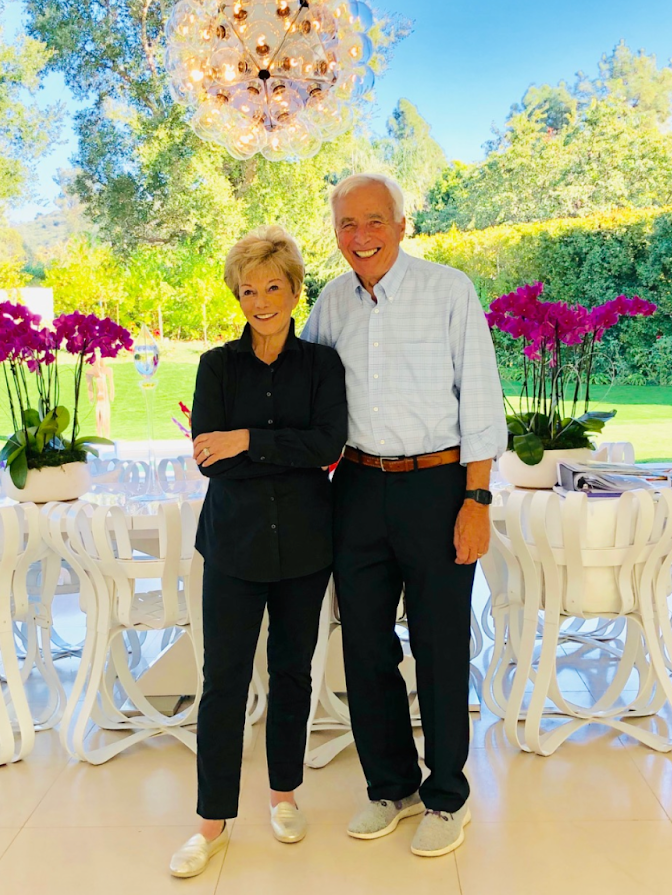 Aris Demetrios and his wife Ilene Nagel pose for the camera in front of tables.