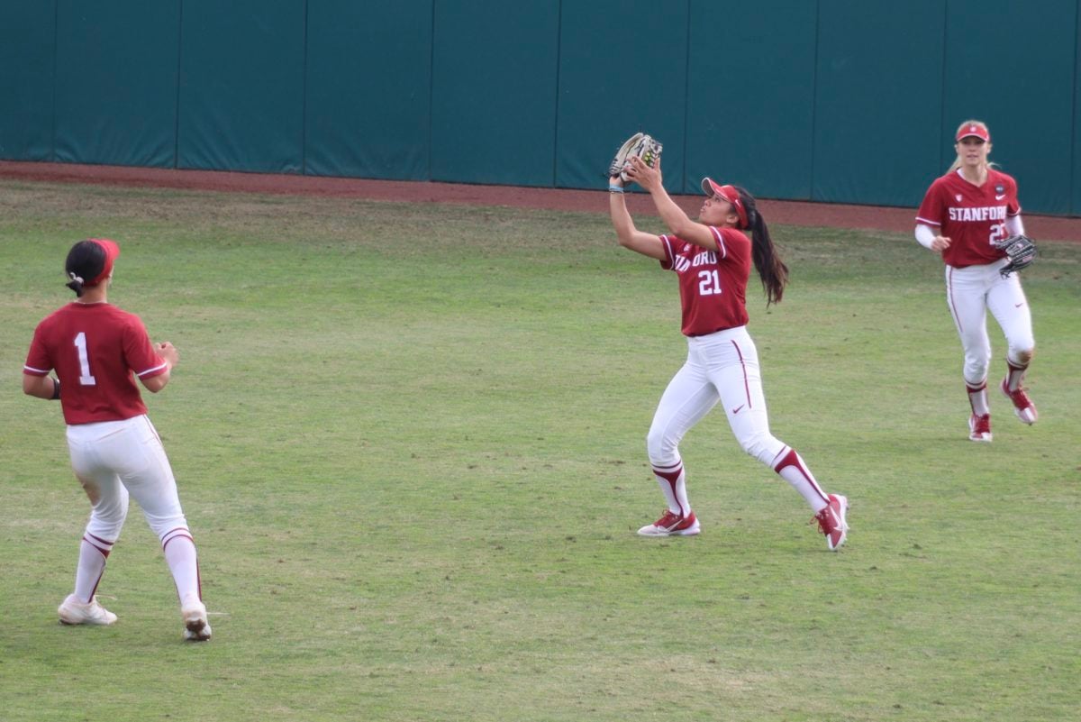 Three players are in the outfield, with two watching as one waits to catch a ball.