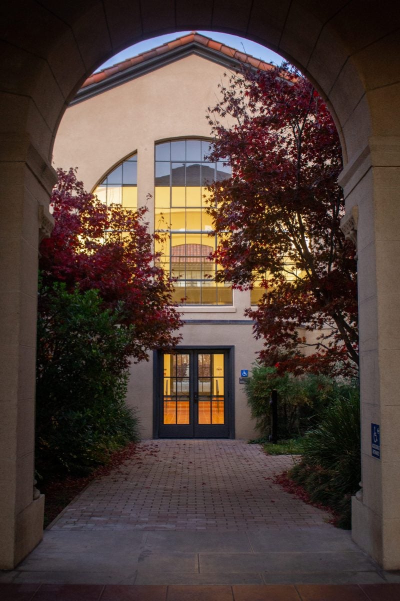 An archway that leads to a building entrance with red and green-leaved trees in between.