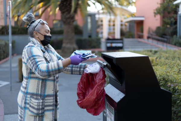 Woman dropping off several COVID-19 tests at a drop-off box. She's wearing a coat and holding a biohazard bag.