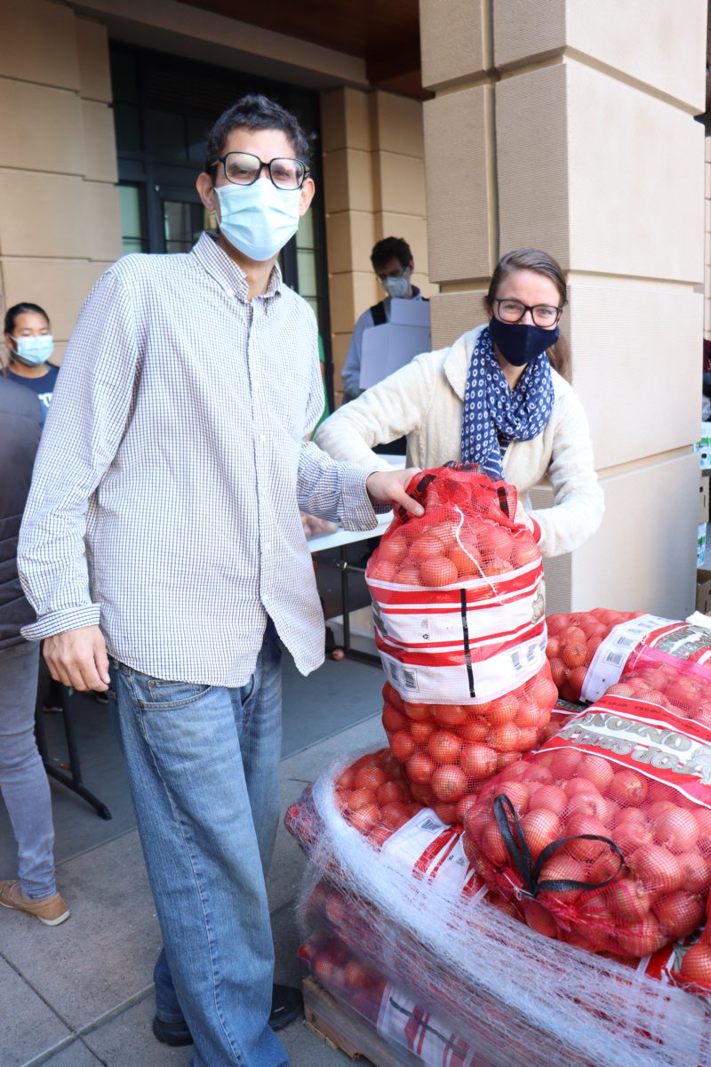 Two masked volunteers with a new bag of onions