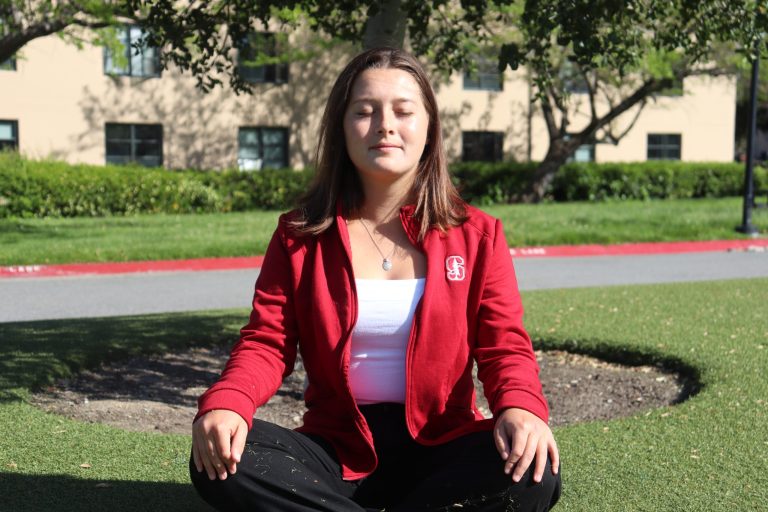 A girl sits cross-legged on the grass with her eyes closed