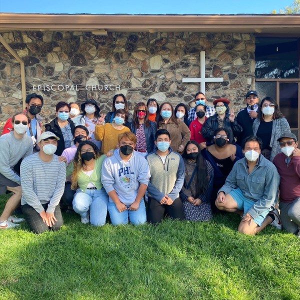 Students with workers and executive committee members of PAWIS (Pilipino Association of Workers and Immigrants) in front of the side of a brick building with a large cross and a sign that reads "Episcopal Church"