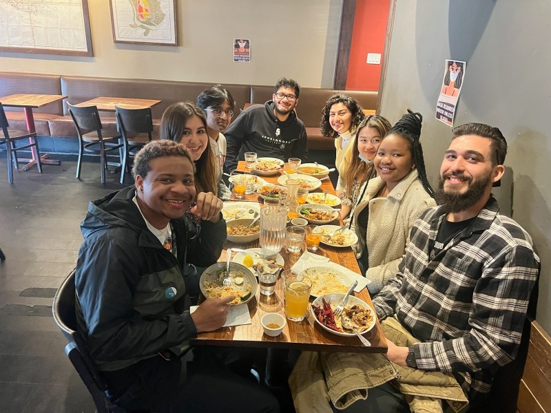 A group of students smile as they sit around a dining table.