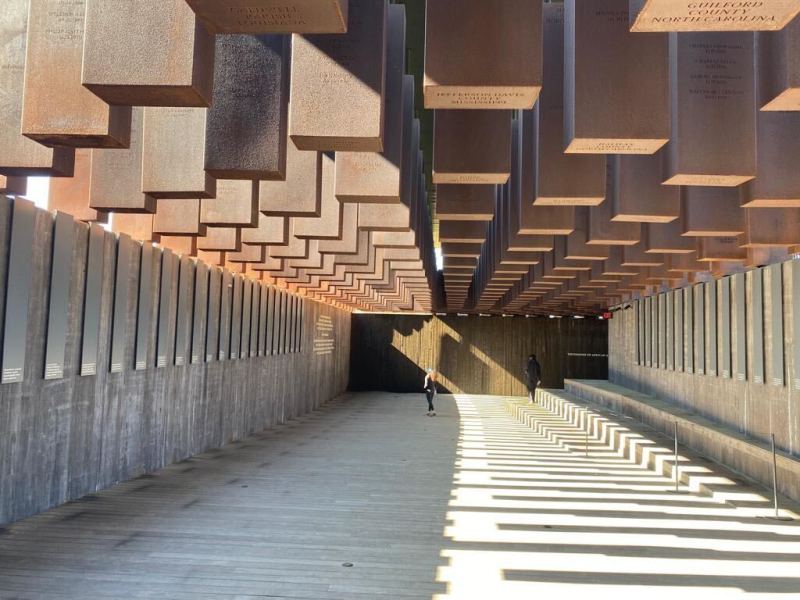 The National Memorial for Peace and Justice at the Equal Justice Initiative’s Legacy Museum. A large open concrete room with many rectangular structures coming down from the ceiling.