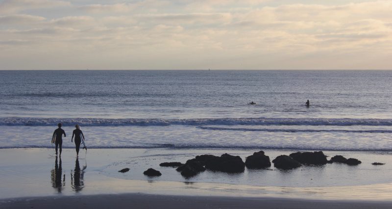 Two silhouettes in the distance on a beach looking away to the ocean.