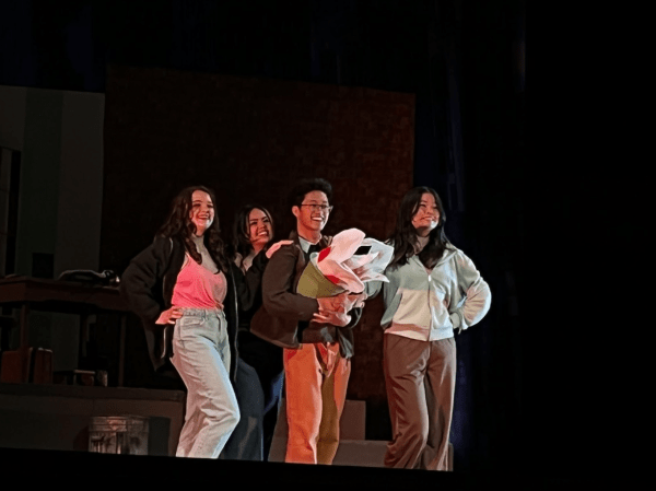 Four cast members stand together on stage.