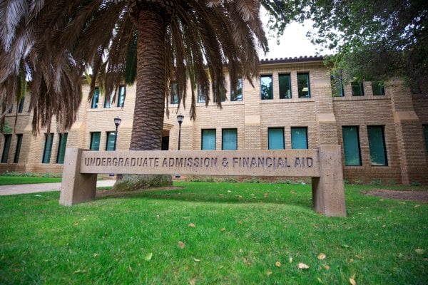 a concrete sign reading 'UNDERGRADUATE ADMISSION & FINANCIAL AID' in front of a palm tree and a brick building