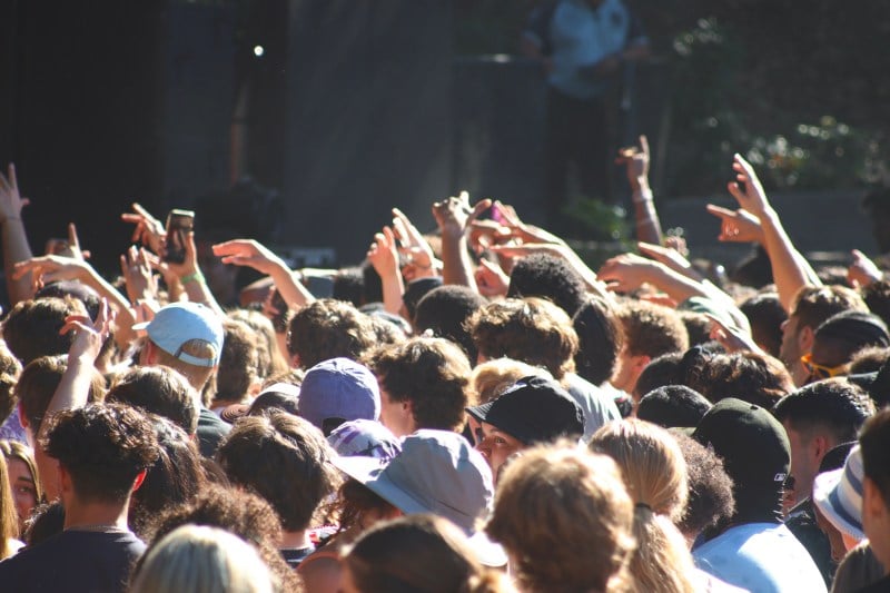 A crowd of attendees stand on the field of Frost Amphitheater with their hands in the air.