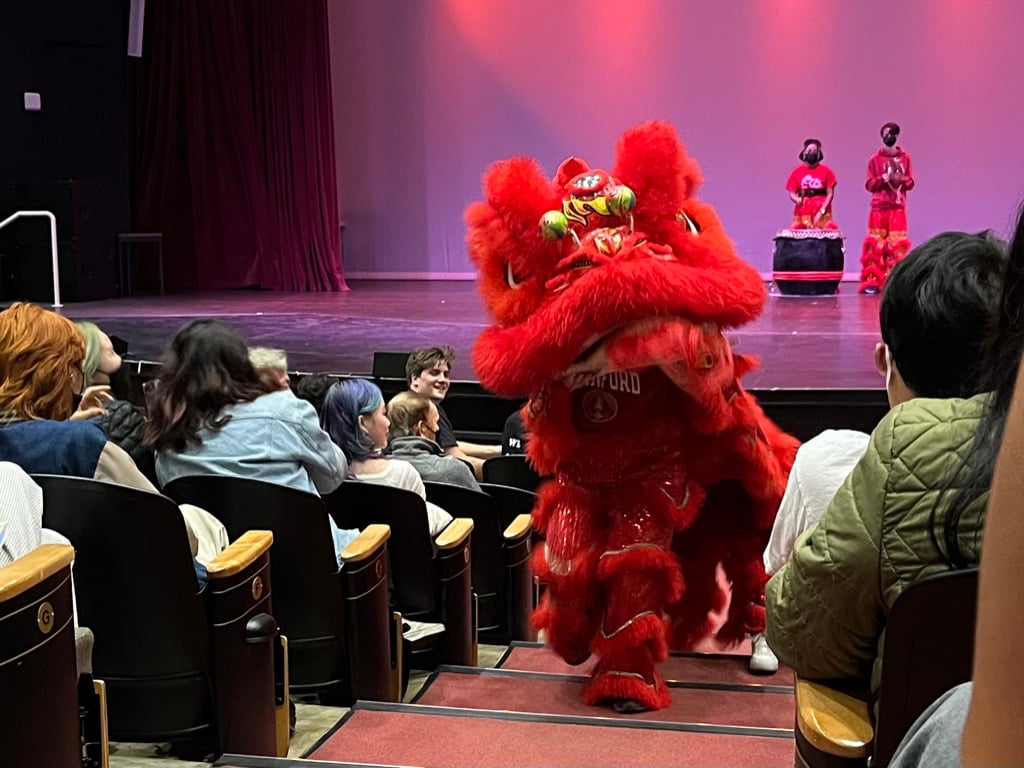 A life sized red lion puppet operated by two students walks up the aisle of Dinkelspiel Auditorium