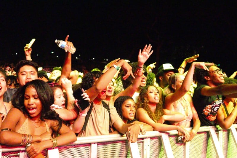 crowd shot of dozens of concertgoers singing along, leaning on barrier and arms outstretched facing frost stage