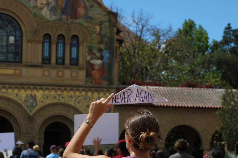 A woman holds a hanger that reads "never again" in front of Stanford Memorial Church