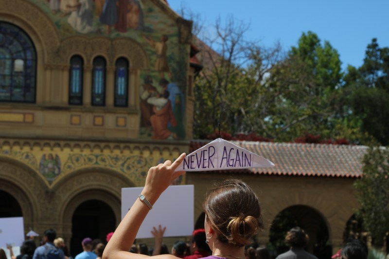 A woman holds a coat hanger that has the words "never again" written over it. 