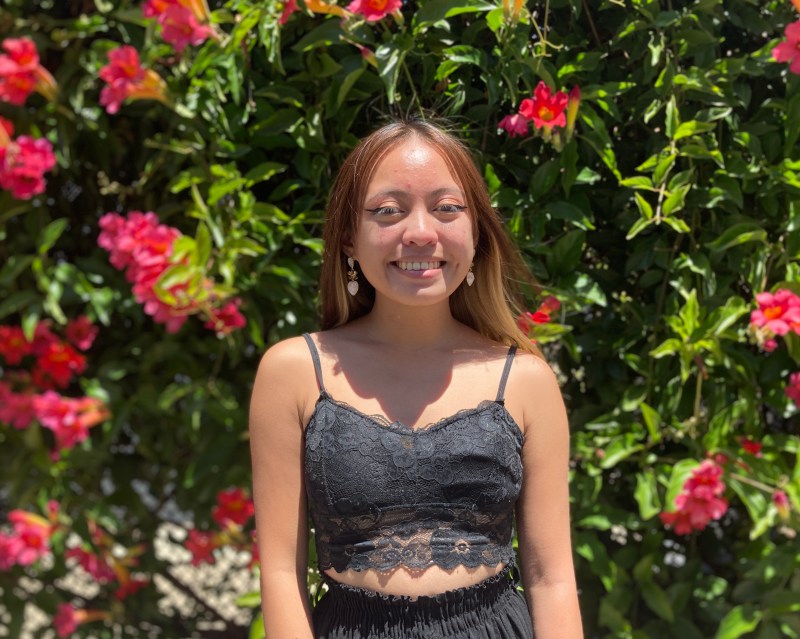 Image of Kiara Fufunan '25 smiling in front of a bush with flowers. 