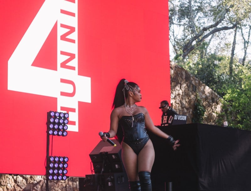 Blackfest opener Day Sulan performs on stage. She wears a black one-piece and her hair is tied into a ponytail. Purple lights and a large red sign reading "4 HUNNID" are in the background.