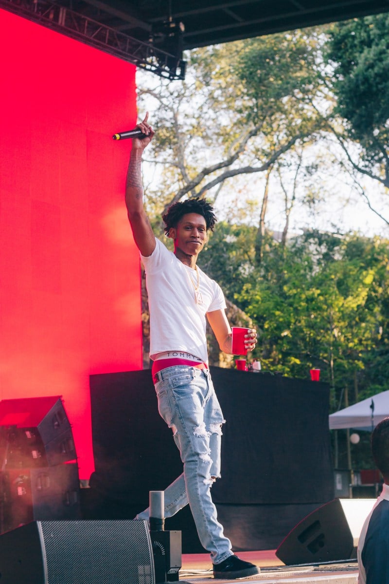 Blackfest opener D3SZN performs on stage. He wears a t-shirt and jeans and is holding up his right hand while looking at the crowd.