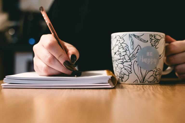 Shot of writer writing with one hand and a mug in the other