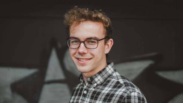 a young adult with short curly hair, glasses, and a plaid shirt