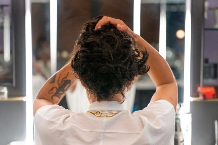 A person sitting in front of a mirror with their hands in their hair.