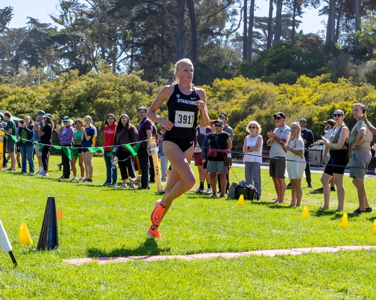 A runner crosses the finish line with people cheering behind her.